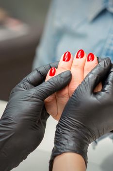 Examination of manicured fingernails. Hands of manicure master in black gloves examining female red nails in manicure salon