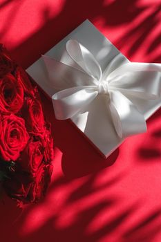 Happy holidays, luxe shopping and love gifts concept - Luxury holiday silk gift box and bouquet of roses on red background, romantic surprise and flowers as birthday or Valentines Day present