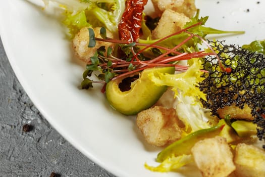 Avocado salad with baby spinach and pomegranate on a black plate on a slate,stone or concrete background.Top view with copy space.