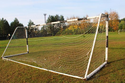 Old football goal against the background of the football field and autumn forest