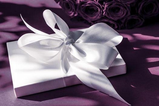 Happy holidays, luxe shopping and love gifts concept - Luxury holiday silk gift box and bouquet of roses on purple background, romantic surprise and flowers as birthday or Valentines Day present