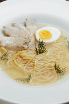 Chicken soup with noodles and vegetables in white bowl.