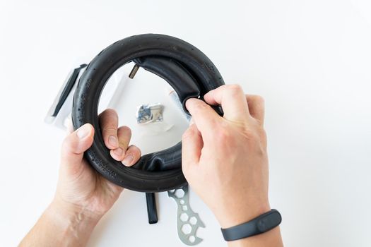 A man carefully looks at the carving of the tire of an electric scooter, fixing a puncture, the master applies a patch and inserts the tire into the wheel on a white background. Vehicle. Repair, fix a puncture