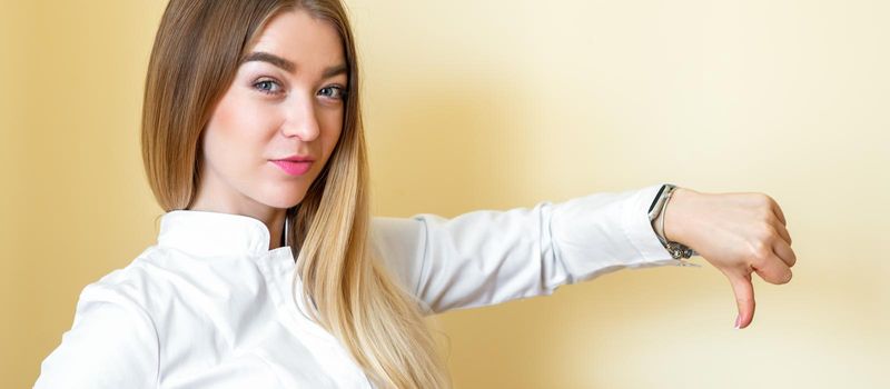 A woman showing dislike. Young beautiful businesswoman wearing a white shirt with thumb down isolated over a yellow background