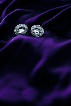 Jewellery brand, elegant fashion and bridal luxe gift concept - Luxury diamond earrings on dark violet silk fabric, holiday glamour jewelery present