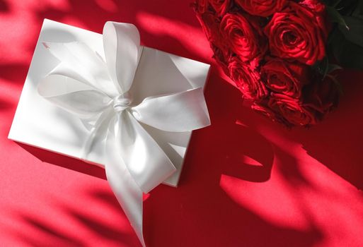 Happy holidays, luxe shopping and love gifts concept - Luxury holiday silk gift box and bouquet of roses on red background, romantic surprise and flowers as birthday or Valentines Day present