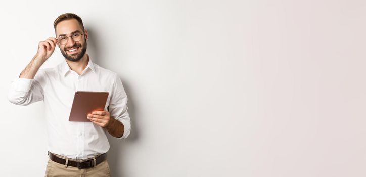 Confident business man working on digital tablet, smiling happy, standing over white background.