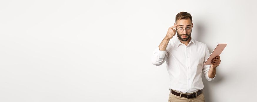 Displeased employer scolding staff while checking report on digital tablet, pointing at head and looking disappointed, standing over white background.