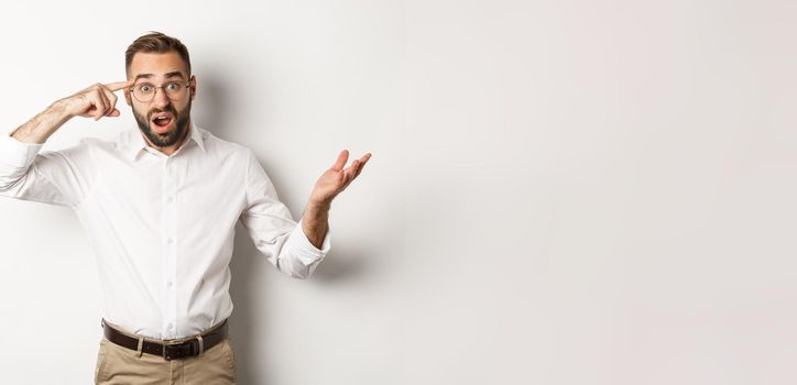 Confused and shocked man pointing at head, scolding employee for acting stupid, standing over white background.