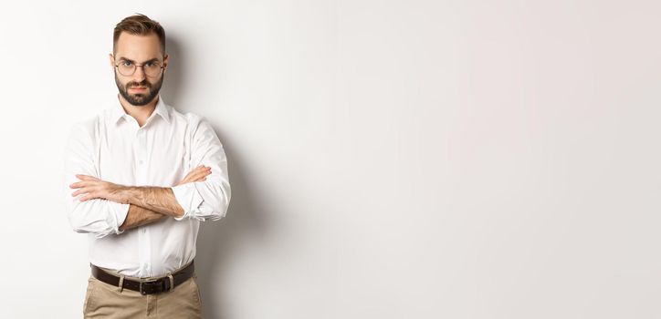 Angry manager looking disappointed, cross arms on chest and frowning displeased, standing over white background. Copy space