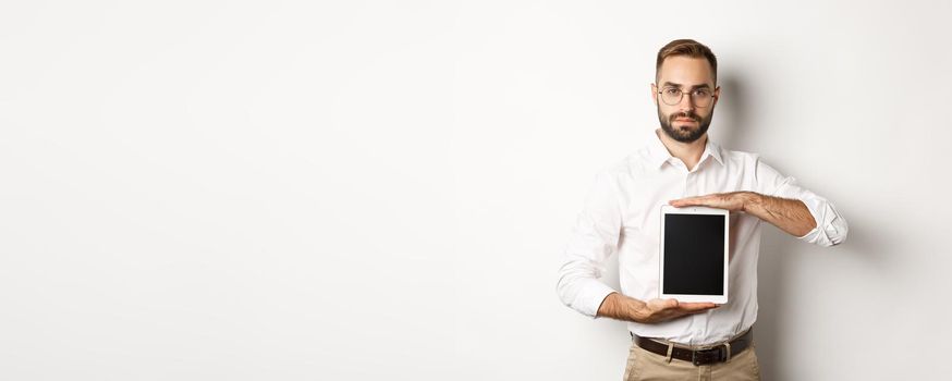 Confident bearded man showing digital tablet screen, demonstrating app, standing over white background.