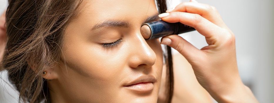 Make up artist contouring the face of a young woman with cream blush close up