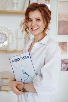 A business woman with a book on Human Design in her hands. A human design specialist works at home. Working at home during the epidemic