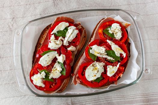 two ham, tomato and mozzarella toasts, ready to be baked, top view