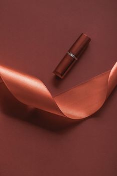 Cosmetic branding, glamour lip gloss and shopping sale concept - Luxury lipstick and silk ribbon on bronze holiday background, make-up and cosmetics flatlay for beauty brand product design