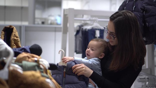 A young woman with a baby in a children's clothing store. Mom in glasses with her son in the mall. 4k