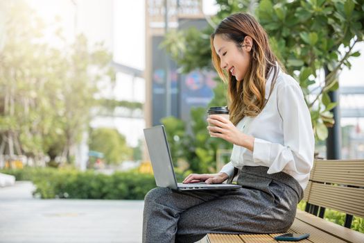 Successful Asian business young woman working laptop outdoor corporate building exterior, Happy professional smiling businesswoman sitting alone typing computer outside street city near office