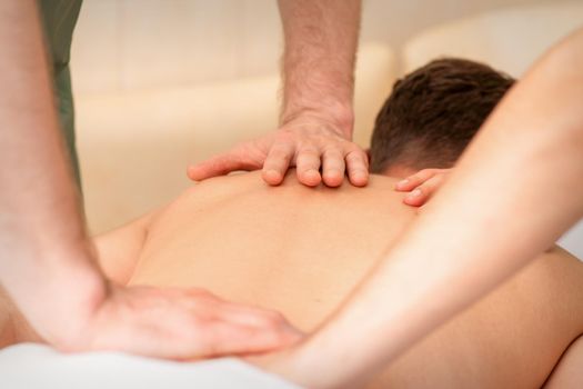 Young man receiving back massage in four hands in spa beauty salon