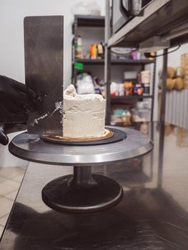 Decorator using spatula and scraper to smooth buttercream on a frosted cake