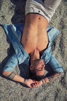 Stylish handsome young man laying on sand at the beach, with eyes closed in the sunlight