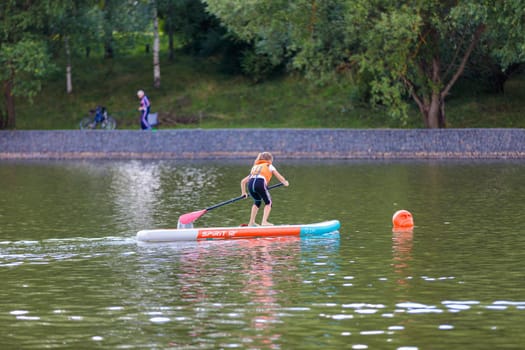 A child swims on a surfboard, pushing off with a paddle. Paddleboarding. Russia Zelenograd 14 August 2021