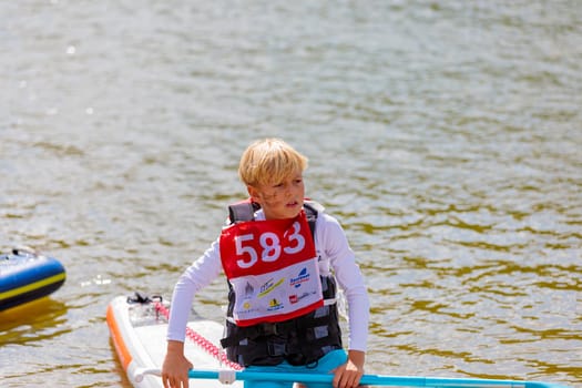 A child swims on a surfboard, pushing off with a paddle. Paddleboarding. Russia Zelenograd 14 August 2021