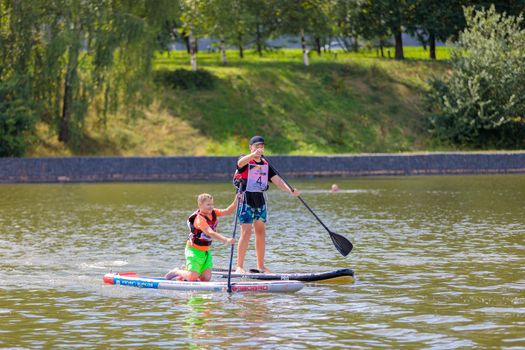 A child swims on a surfboard, pushing off with a paddle. Paddleboarding. Russia Zelenograd 14 August 2021