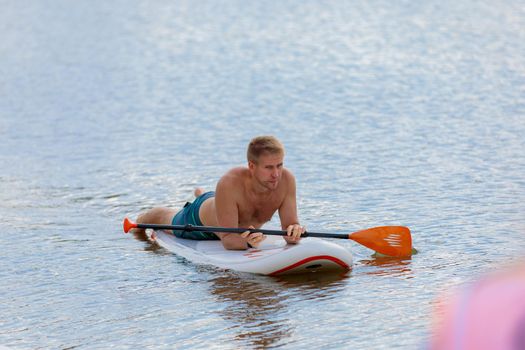 An adult man swims on a surfboard lying down, pushing off with a paddle. Paddleboarding. Russia Zelenograd 14 August 2021