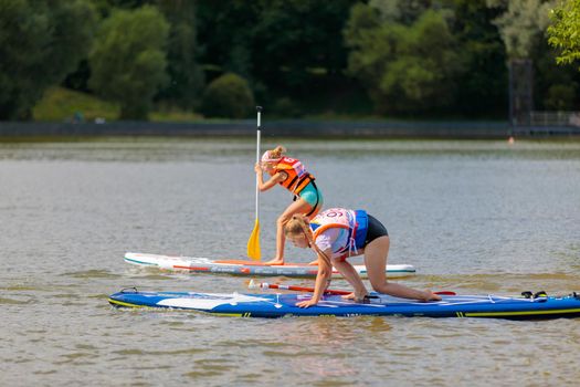 A child swims on a surfboard, pushing off with a paddle. Paddleboarding. Russia Zelenograd 14 August 2021