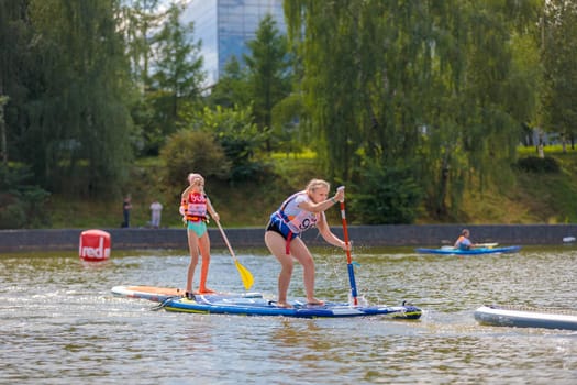 A child swims on a surfboard, pushing off with a paddle. Paddleboarding. Russia Zelenograd 14 August 2021