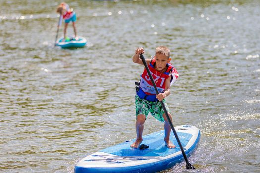 A child swims on a surfboard, pushing off with a paddle. Paddleboarding. Russia Zelenograd 14 August 2021