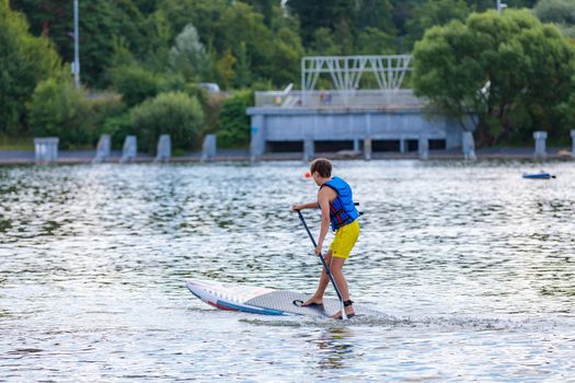 A child swims on a surfboard, pushing off with a paddle. Paddleboarding. Russia Zelenograd 14 August 2021