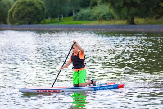 A child swims on a surfboard, pushing off with a paddle. Paddleboarding. Russia Zelenograd 14 August 2021