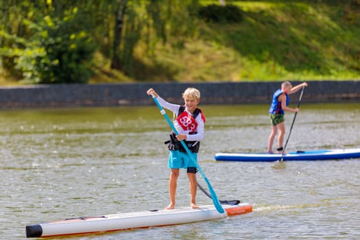 A child swims on a surfboard, pushing off with a paddle. Paddleboarding. Russia Zelenograd 14 August 2021