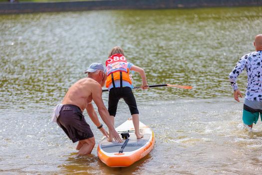 A child swims on a surfboard, pushing off with a paddle. Paddleboarding. Russia Zelenograd 14 August 2021