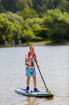 An adult man swims on a surfboard, pushing off with a paddle. Paddleboarding. Russia Zelenograd 14 August 2021