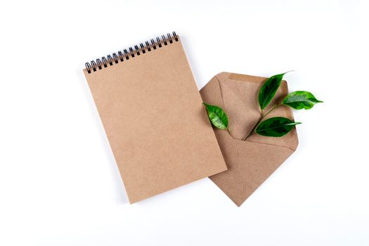 A notepad and an envelope made from recycled paper lie on a white surface with a sprig of a green plant. The concept is ecology, nature conservation, recycling, no waste. Selective focus. Copy space.
