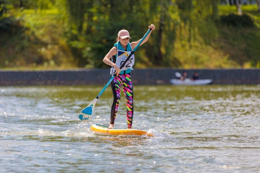 A child swims on a surfboard, pushing off with a paddle. Paddleboarding. Russia Zelenograd 14 August 2021