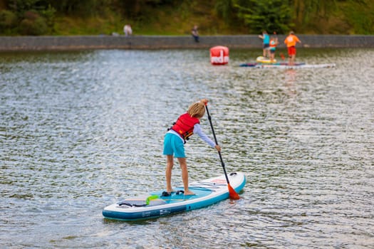 A child swims on a surfboard, pushing off with a paddle. Paddleboarding. Russia Zelenograd 14 August 2021