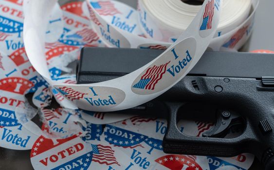 Concept for election violence with handgun placed on many torn and damaged voting stickers or buttons
