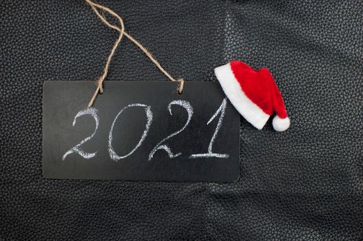 2021 - chalkboard with outlined text and Santa hat on black leather background