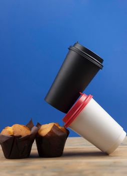 Classic banana nut muffins in black paper wrapper with disposable paper coffee cups on wooden table. 