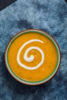 Autumnal spiced carrot and coriander soup with a swirl of cream on blue and black tabletop