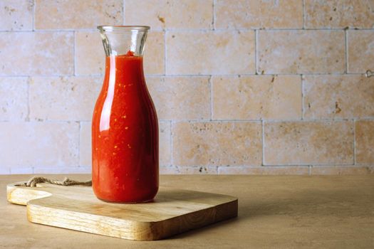 A glass jar bottle with homemade tomato sauce stands on a wooden cutting board on the table. Selective focus. Copy shace.