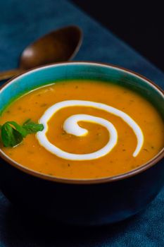 Autumnal spiced carrot and coriander soup with a swirl of cream on blue and black tabletop