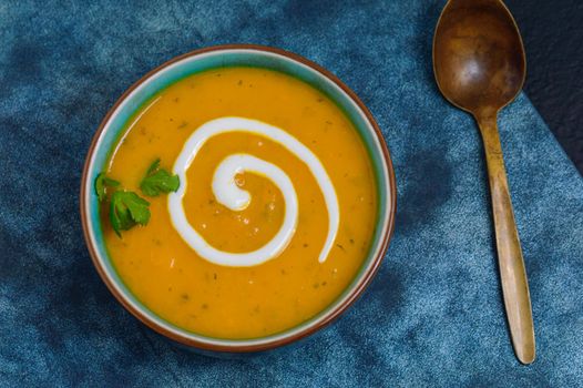 Autumnal spiced carrot and coriander soup with a swirl of cream on blue and black tabletop