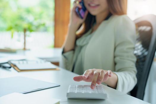 Portrait of an Asian bank employee using a financial budget calculator, notepad, telephone and computer to working.