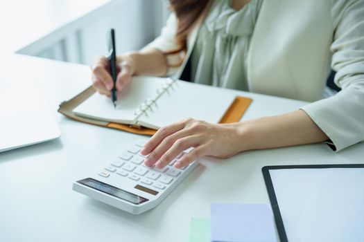 Portrait of an Asian bank employee using a financial budget calculator, notepad and computer to working.