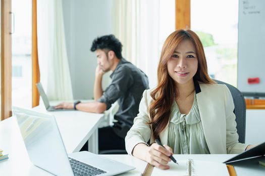 Portrait of an Asian bank employee using notebooks to take notes, budget documents and computers to close financial statements.