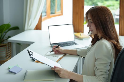 Portrait of an Asian bank employee using notebooks to take notes, budget documents and computers to close financial statements.